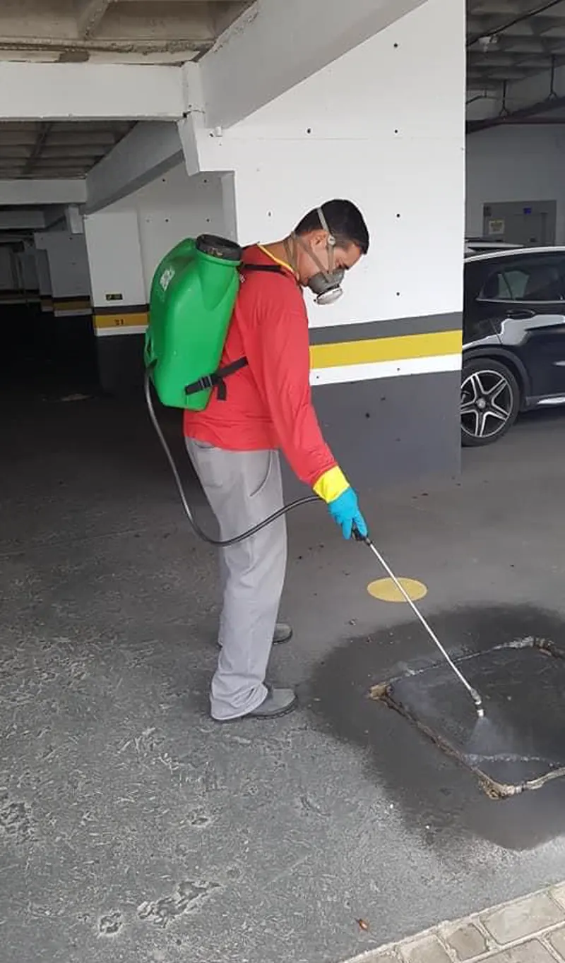 Técnico da El Shaday Dedetizadora aplicando produto com pulverizador costal na garagem de um prédio em Cuiabá